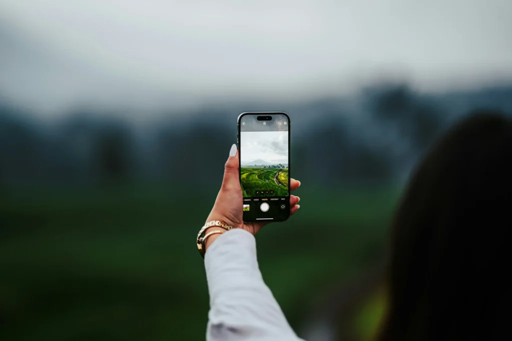 Image of a person's hand taking a photo with their cell phone of a green landscape