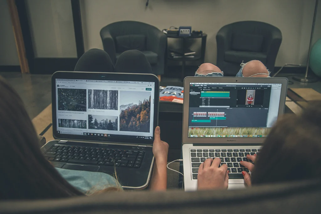 Image of two computes on two people's laps from behind each working on different projects