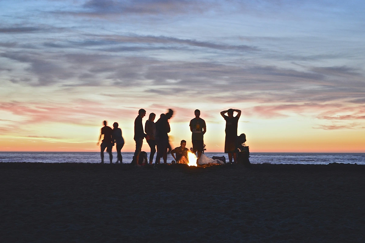 Image of nine friends on a beach at sunset with a campfire