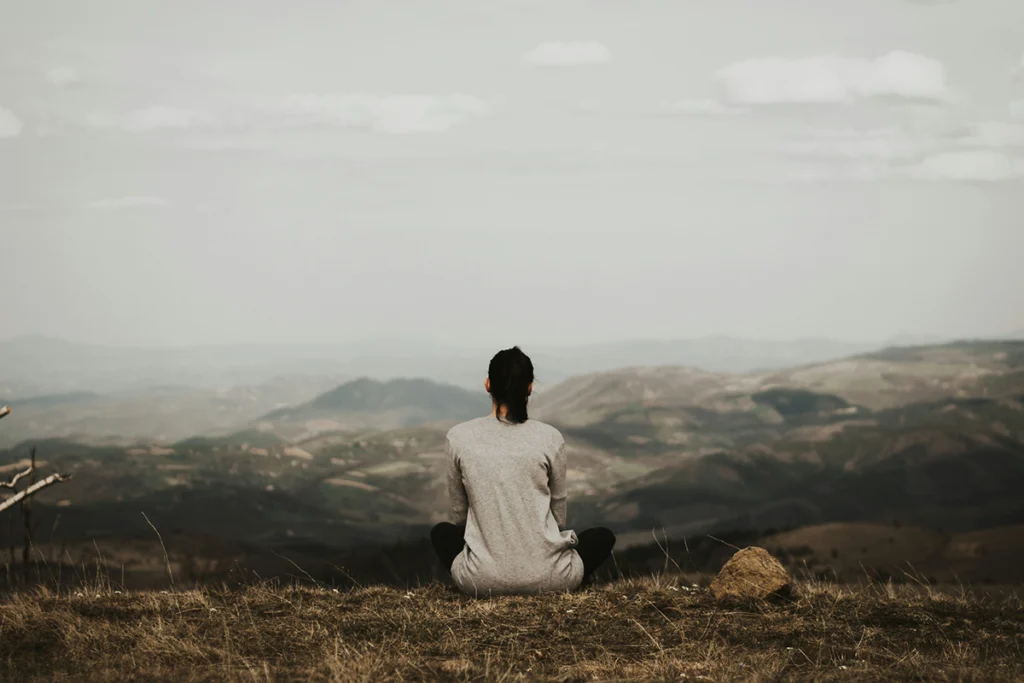Image of a person sitting looking at the view with mountains in a meditative pose