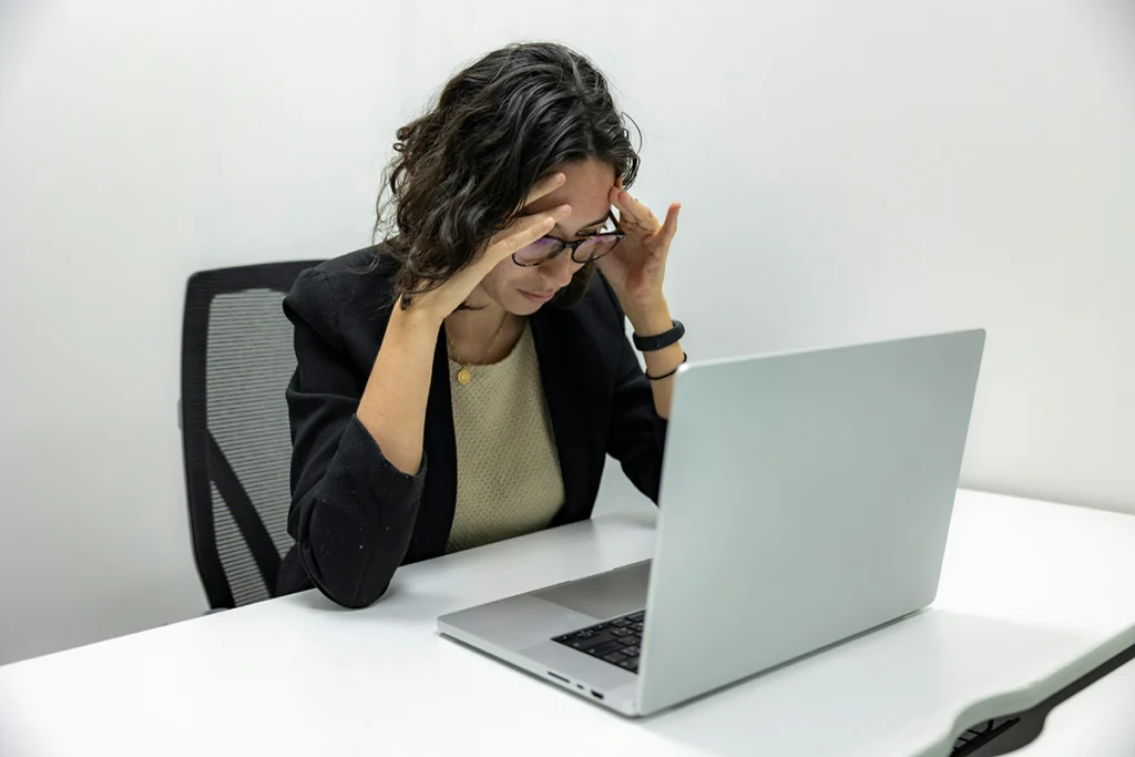 Image of person sitting at a desk with hands on their forehead looking at a laptop