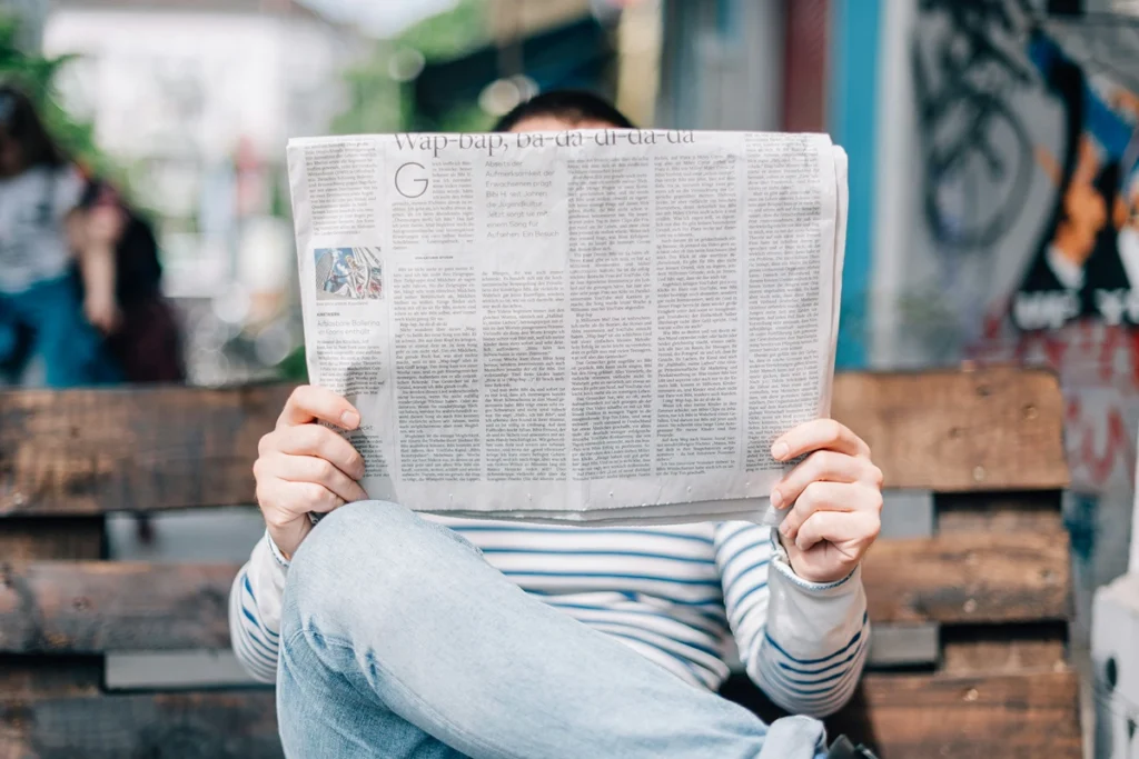 Image of person sitting on bench reading a newspaper with their face covered