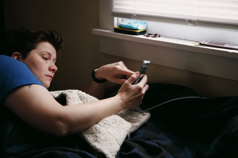 Image of a person in bed on their cell phone as it is plugged into the wall