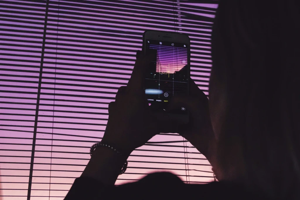 Silhouette of a person taking a photo of the sunset on their phone camera.