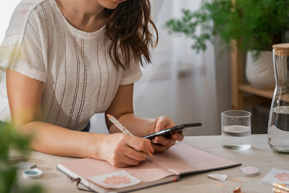 Image of person on their phone and writing on physical journal