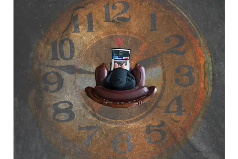 Overhead view of a person sitting on a chair on their computer with a design on the floor of a clock.