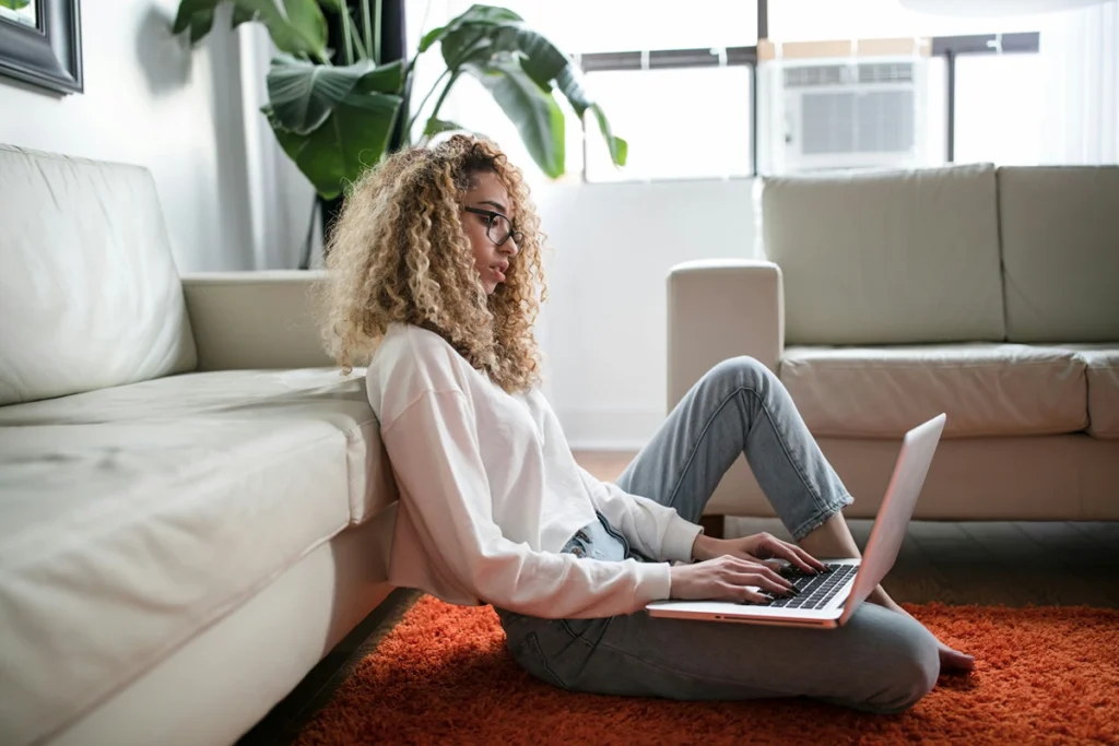Image of person sitting in home on the carpet looking at their laptop computer
