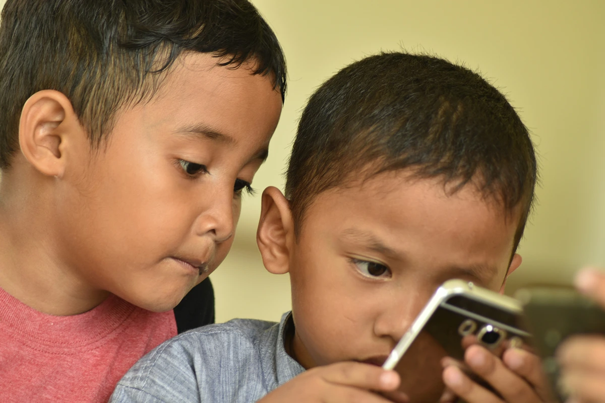Image of two children looking up close at a cell phone