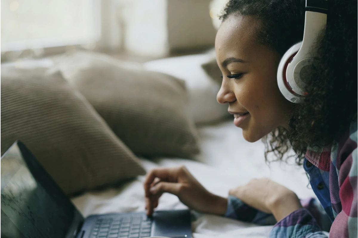 Image of teenager in bed on their laptop with headphones on