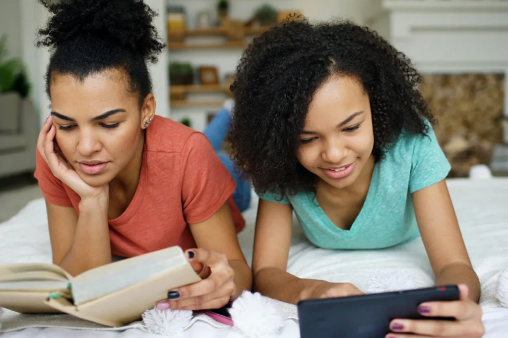 Image of two people: one reading a book the other on a phone