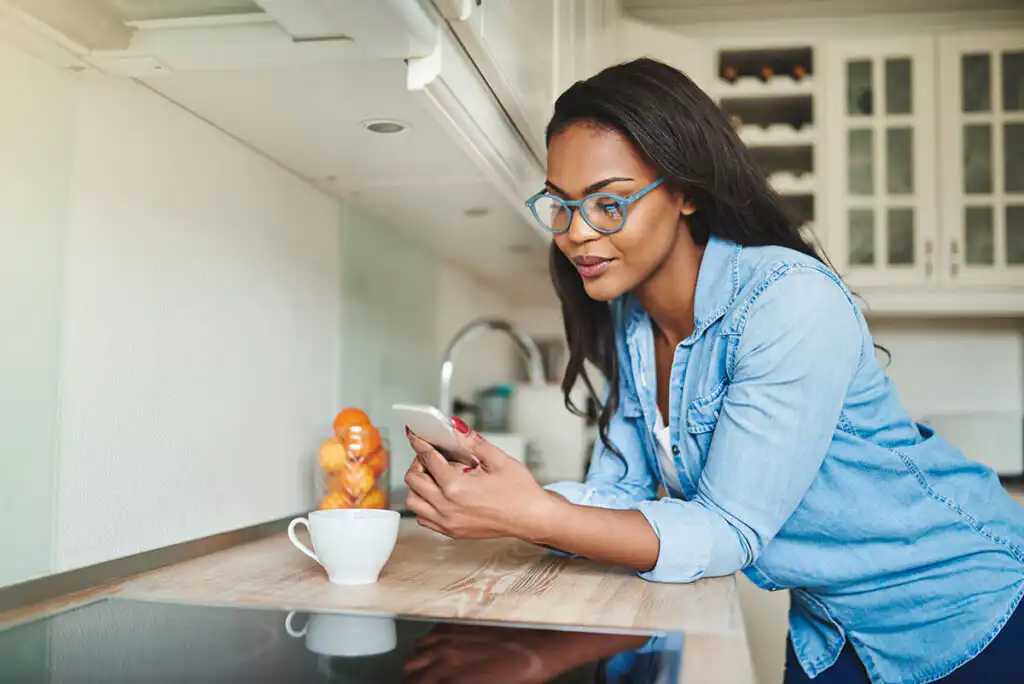 Woman at a kitchen counter in the morning reading her phone beside a cup of coffee