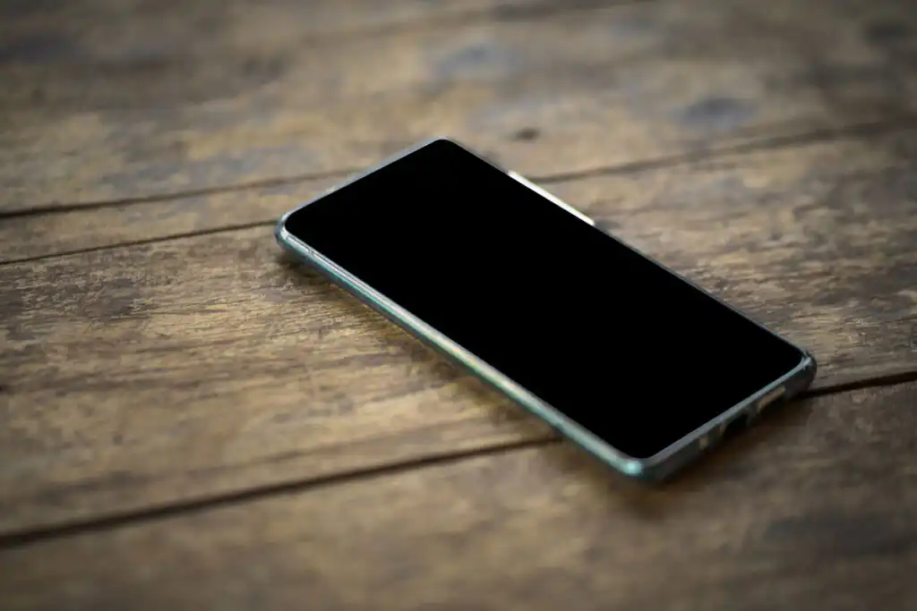 A phone with a dark screen lying on a wooden table