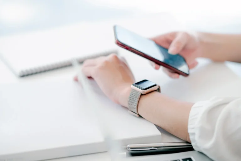 A woman's hand with a smartwatch holding a phone at a desk
