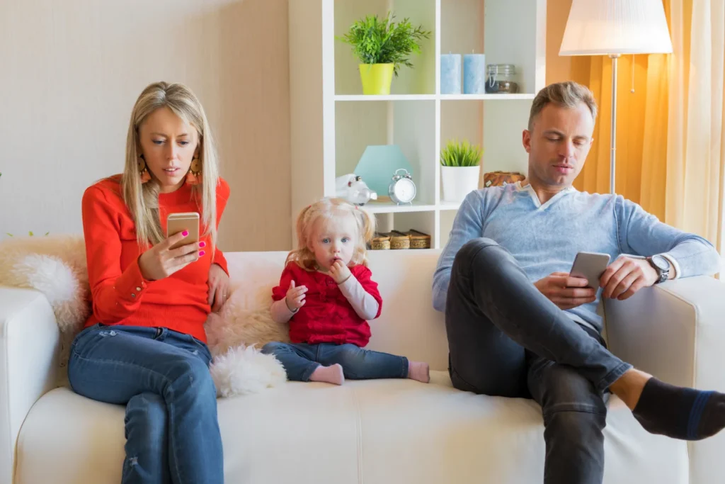 Two parents on a couch looking at their phones while their child sits between them