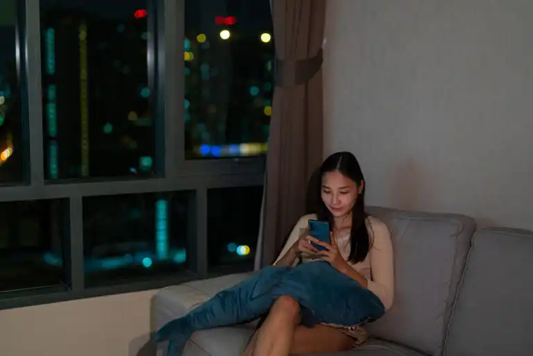 Woman sitting on a couch in a dark living room late at night, looking at her phone