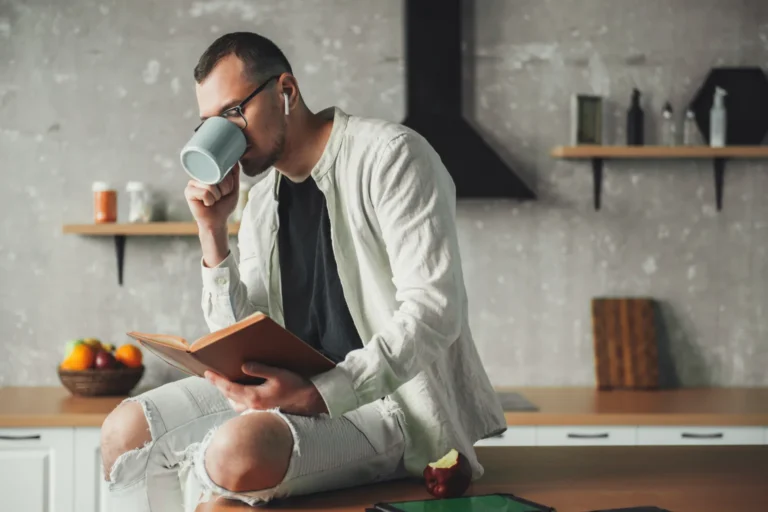A man reading a book with a coffee in a kitchen, no phone in sight