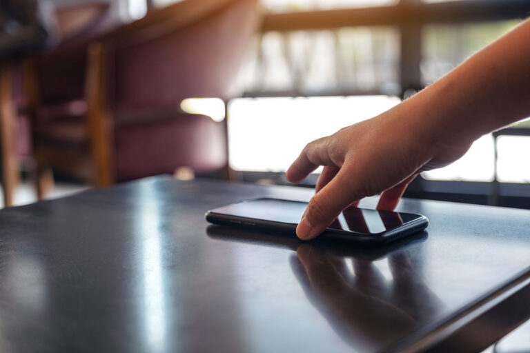 A hand setting a phone with a dark screen down on a table.