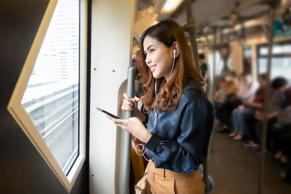 Woman standing on a commuter train by the window, looking down at her phone.