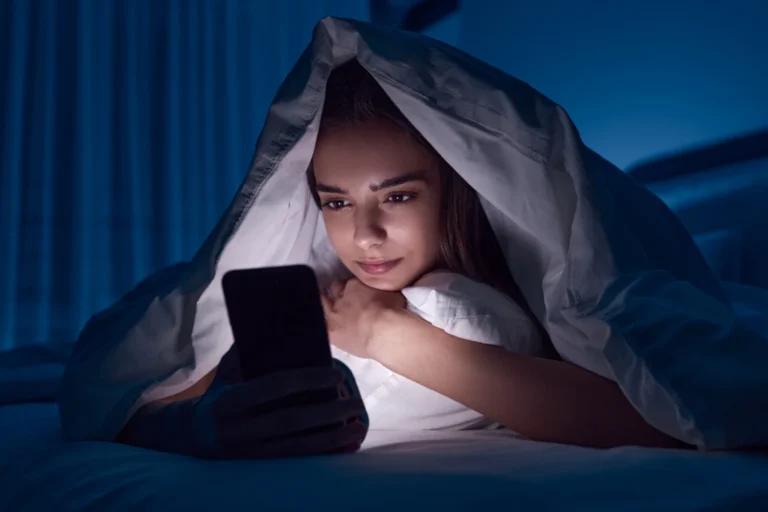 A woman lying in bed at night looking at her phone